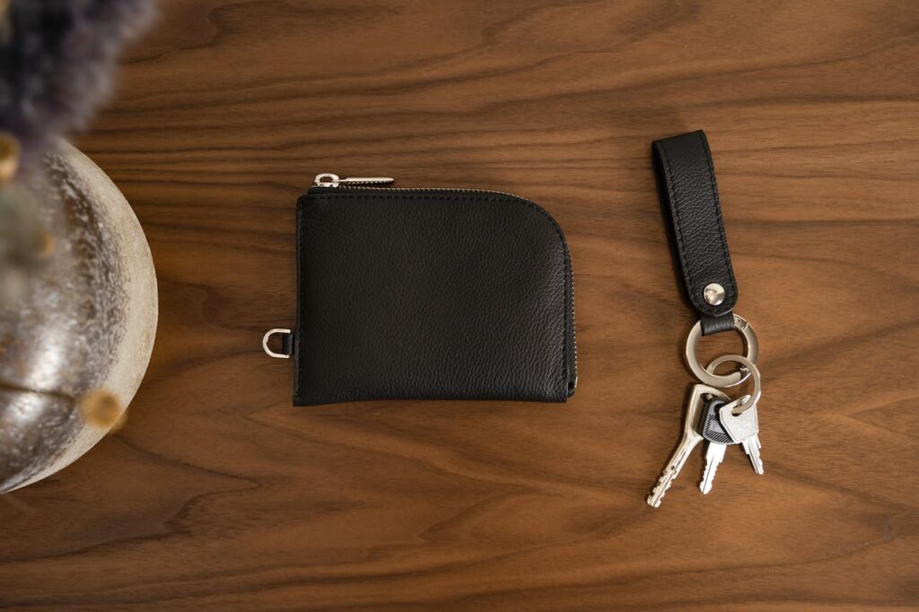 pexels photo 15440419 Close-up of a black leather wallet and keychain with keys on a smooth wooden surface.